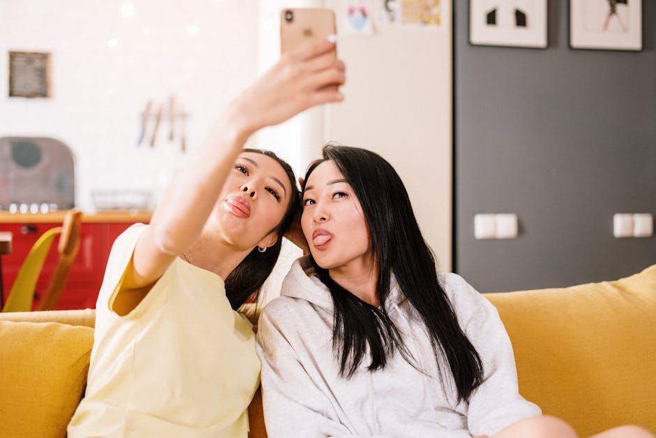 Two friends make funny faces while taking a selfie on a cozy sofa at home.