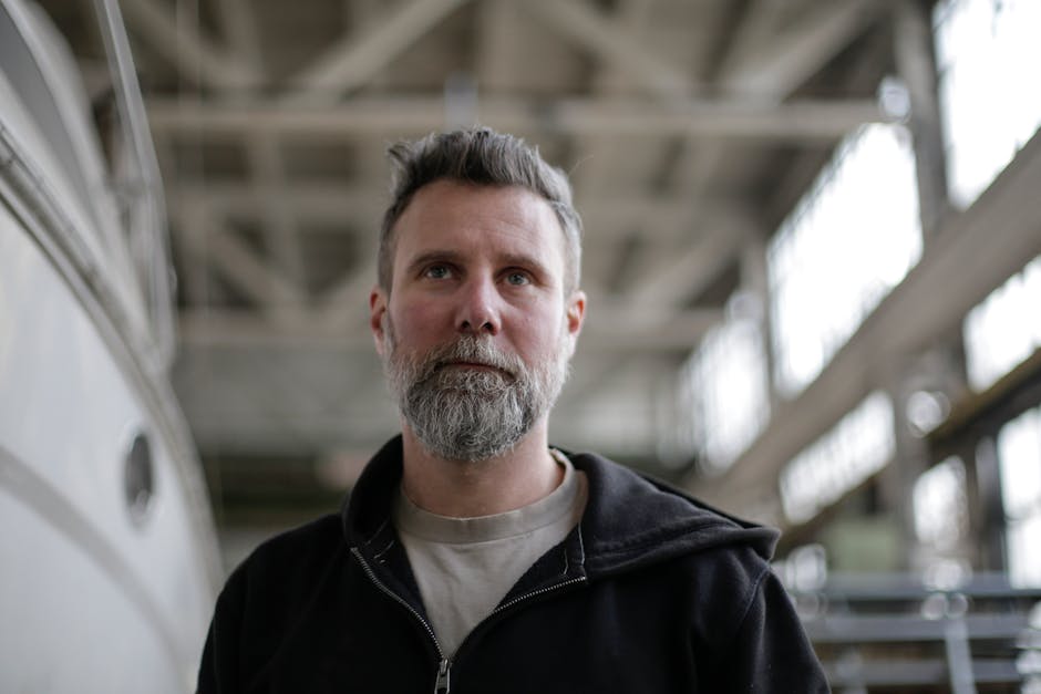 Close-up portrait of a confident man with a beard in an indoor industrial environment.