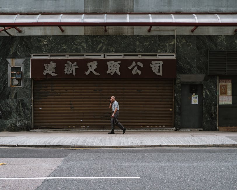 Elderly man walking past a closed shop with Chinese signage on a Hong Kong sidewalk.