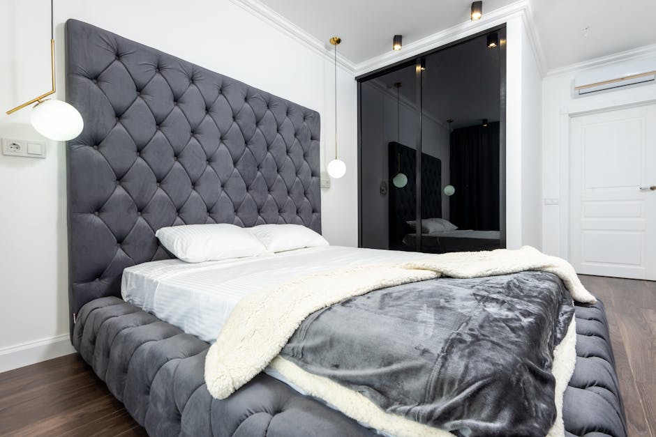 Elegant bedroom showcasing a plush gray headboard with luxurious bedding and contemporary decor.