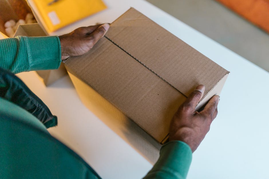 Close-up of hands holding a brown cardboard box on a white table indoors.