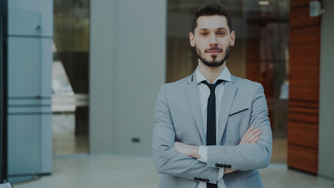 A man in a suit with arms crossed stands confidently.