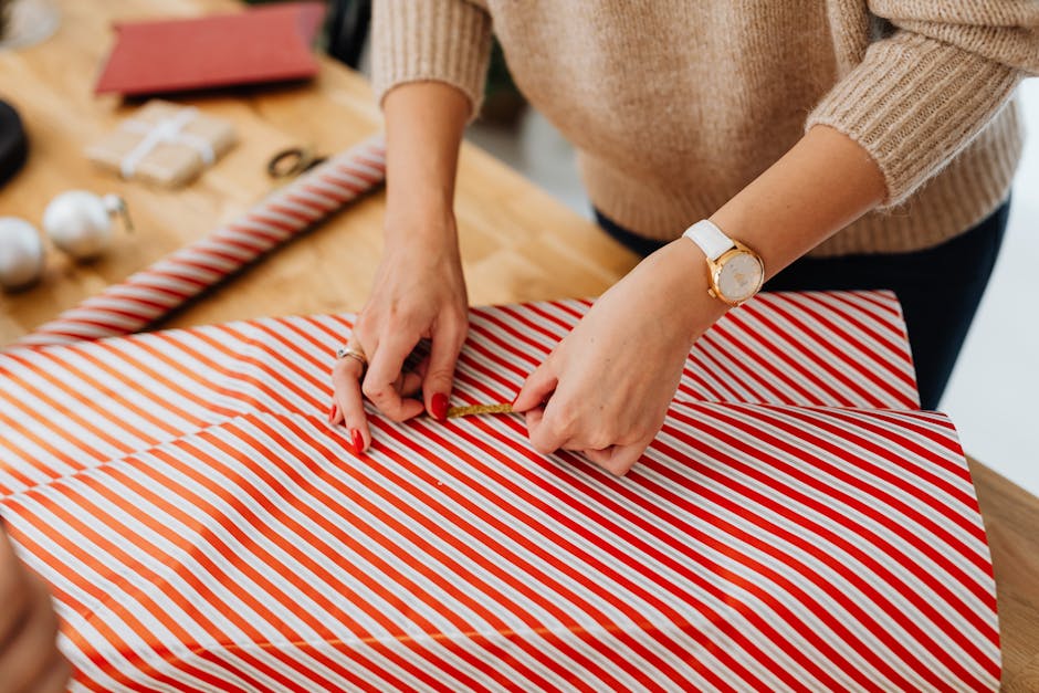 Close-up of a woman wrapping a Christmas gift with red striped paper indoors.