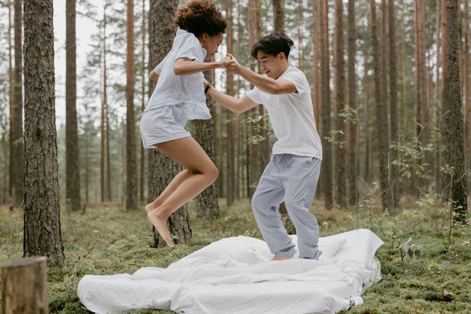 A joyful couple jumping on a bed outdoors in a peaceful forest setting.
