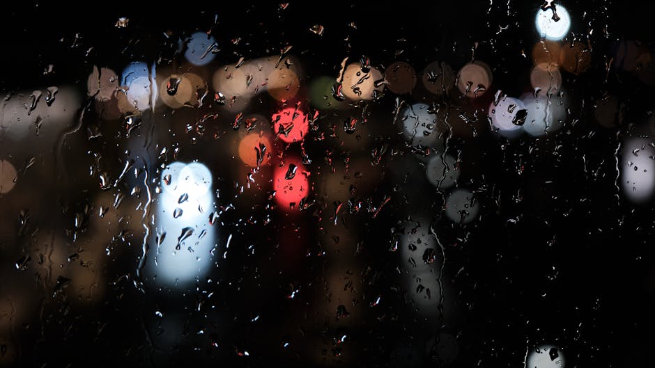 Raindrops on a window at night creating a bokeh effect with colorful city lights.
