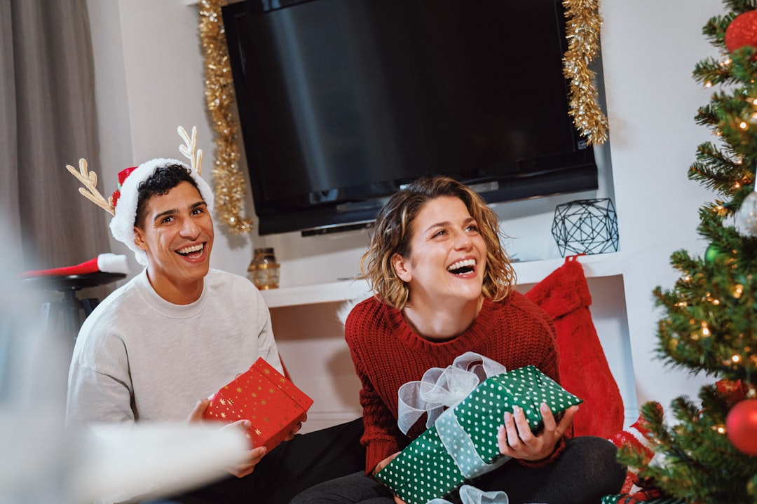 a person and a girl sitting on a couch with presents in front of a christmas tree