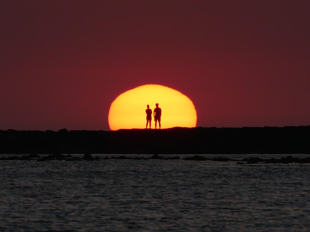 Two silhouetted figures watch the setting sun.
