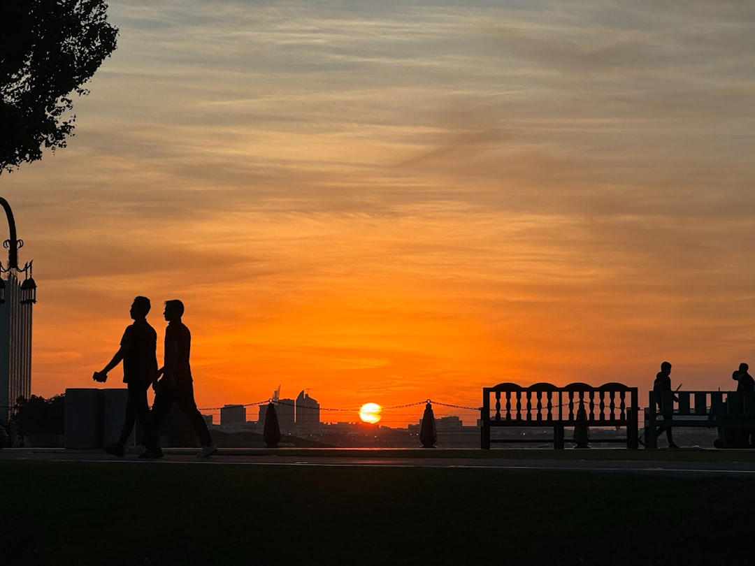 A couple of people walking across a park at sunset