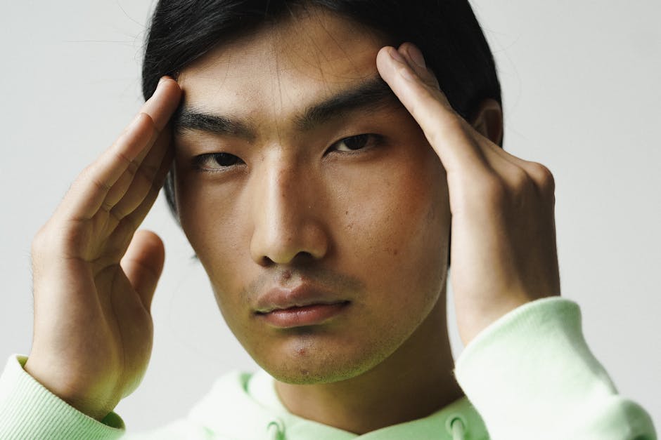 A close-up portrait of a man with hands on his head, conveying deep thought or pain.