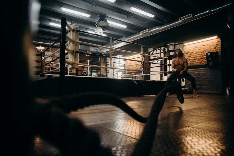Muscular man engaged in intense rope workout inside industrial gym setting.