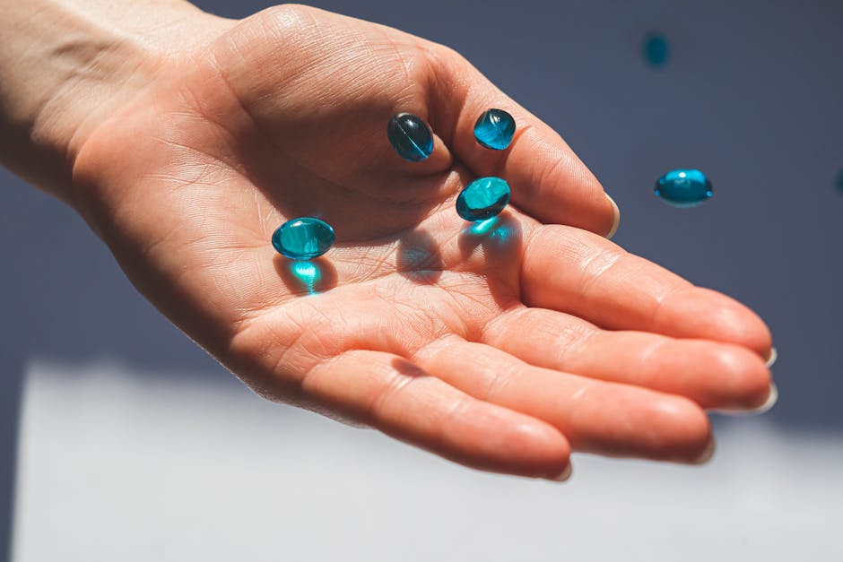 A close-up photo of a hand holding blue capsules, against a neutral background.