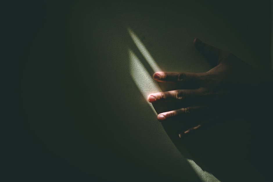 A dramatic hand reaching towards a narrow beam of sunlight against a dark background.