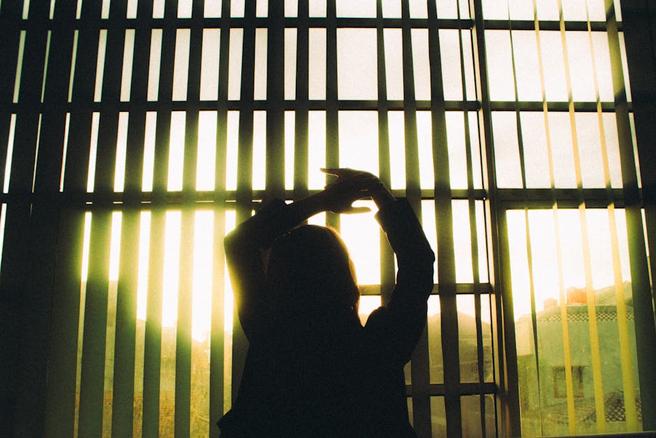 Silhouette of a woman stretching in front of large window blinds with sunlight streaming in.