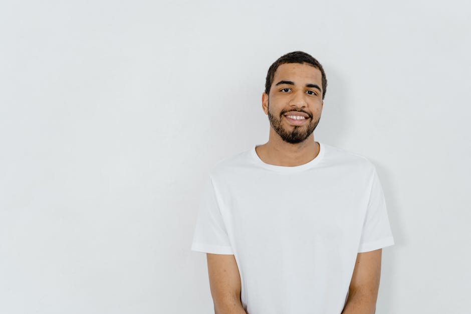 Casual portrait of a smiling man in a minimalist white t-shirt with copy space on a plain background.