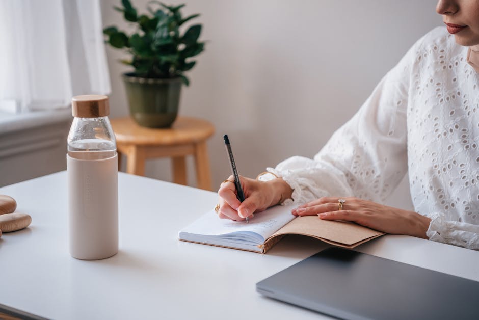 Adult writing in a notebook at a desk, stylish pen and minimalist setup.