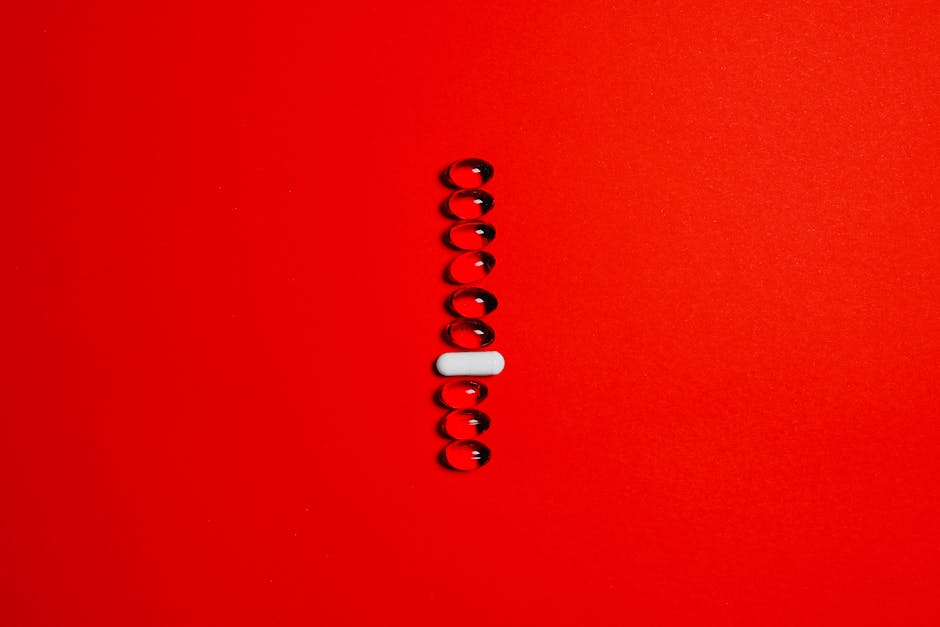 Minimalist setup of a white capsule surrounded by black gel pills on a vibrant red surface.